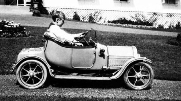 Kong Olav fikk bil allerede som liten gutt. Ikke hvilken som helst bil heller. Dette er nemlig en tro og avansert kopi av en ordentlig Cadillac fra 1912, men med elektrisk motor.Det ble bygget tre slike biler. Kong Olavs var en julegave fra mormor, dronning Alexandra av Storbritannia, i 1912. Den andre fikk prinsen av Siam og den siste bilen fikk barnebarnet til Cadillacs grunnlegger, Wilfred Leland Jr.Det sies at Kong Olav flittig brukte den lille bilen på Bygdøy kongsgårds mange grusganger. (Foto: A.B. Wilse/Det kongelige hoffs fotoarkiv) Kong Olav fikk bil allerede som liten gutt. Ikke hvilken som helst bil heller. Dette er nemlig en tro og avansert kopi av en ordentlig Cadillac fra 1912, men med elektrisk motor.Det ble bygget tre slike biler. Kong Olavs var en julegave fra mormor, dronning Alexandra av Storbritannia, i 1912. Den andre fikk prinsen av Siam og den siste bilen fikk barnebarnet til Cadillacs grunnlegger, Wilfred Leland Jr.Det sies at Kong Olav flittig brukte den lille bilen på Bygdøy kongsgårds mange grusganger. (Foto: A.B. Wilse/Det kongelige hoffs fotoarkiv)