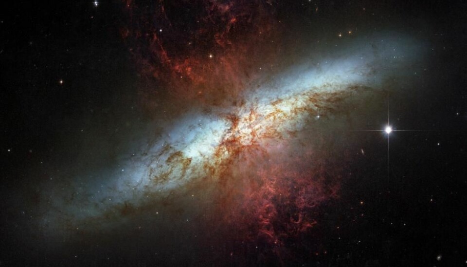 M82 er et eksempel på en veldig aktiv galakse der det dannes og eksploderer massevis av stjerner. Herfra sendes det ut galaktiske vinder av hydrogengass som er markert som røde områder på bildet.  (Foto: NASA/ESA)
