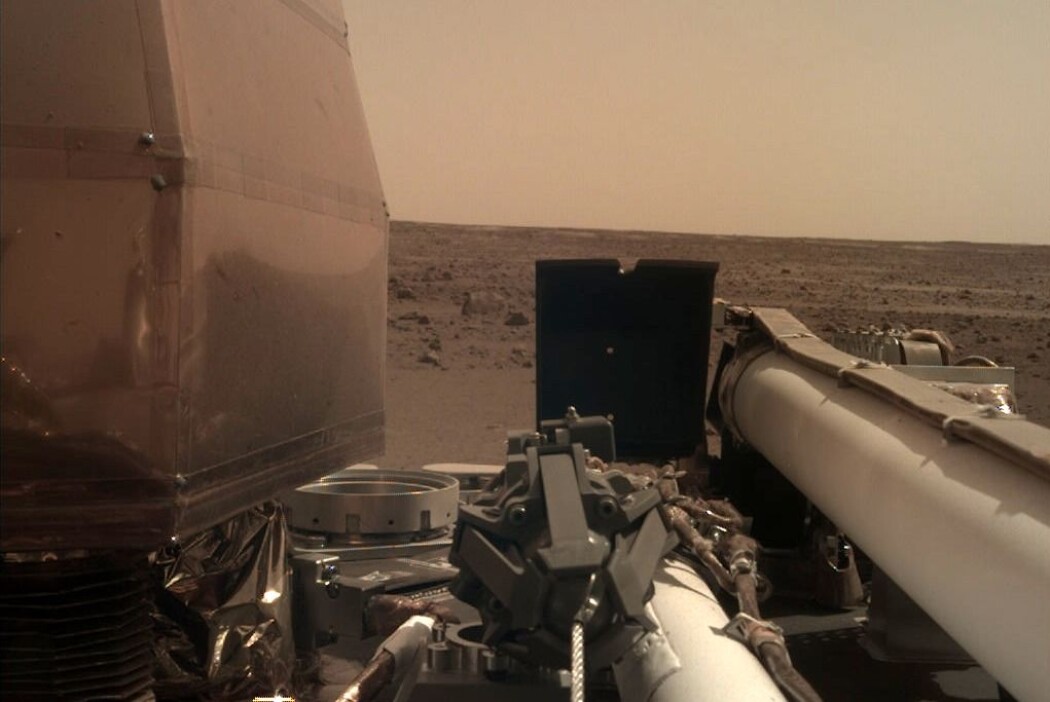 Et Insight-kamera med støvfilter skuer ut over et øde Mars-landskap. Her skal den jobbe i to år. (Foto: NASA/JPL-Caltech) Et Insight-kamera med støvfilter skuer ut over et øde Mars-landskap. Her skal den jobbe i to år. (Foto: NASA/JPL-Caltech)