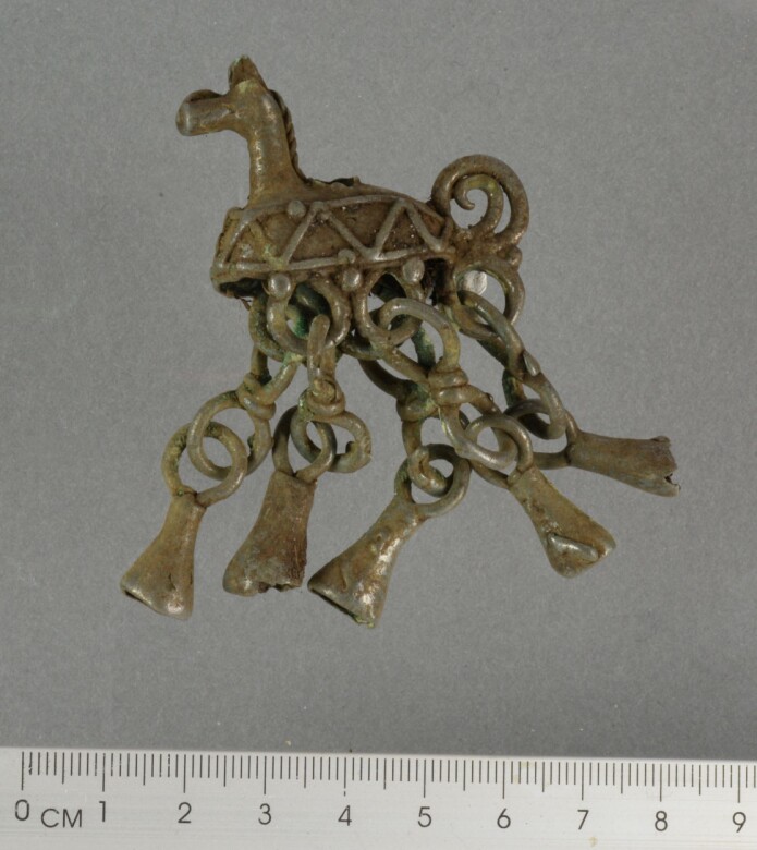 Ts15755. Hengesmykke av bronse fra Øksnes kommune. Hestehode og under kroppen henger det fem lenker med konisk hengeblikk. (Foto: Bente Richardsen Isaksen / Norges arktiske universitetsmuseum) Ts15755. Hengesmykke av bronse fra Øksnes kommune. Hestehode og under kroppen henger det fem lenker med konisk hengeblikk. (Foto: Bente Richardsen Isaksen / Norges arktiske universitetsmuseum)