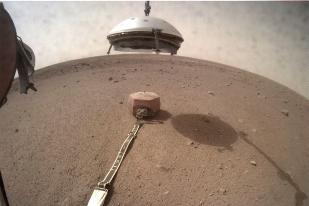 Insights robotarm senker skjoldet ned over seismometeret. (Foto: NASA/JPL-Caltech) Insights robotarm senker skjoldet ned over seismometeret. (Foto: NASA/JPL-Caltech)