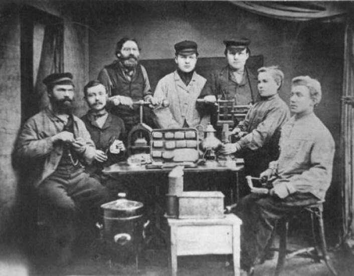 Dette bildet viser Jakob Helvig til venstre og noen av hans ansatte. Hver av personene på bildet illustrerer ett skritt i produksjonen av en håndlaget hermetikkboks. Foto: Norsk Folkemuseum Dette bildet viser Jakob Helvig til venstre og noen av hans ansatte. Hver av personene på bildet illustrerer ett skritt i produksjonen av en håndlaget hermetikkboks. Foto: Norsk Folkemuseum