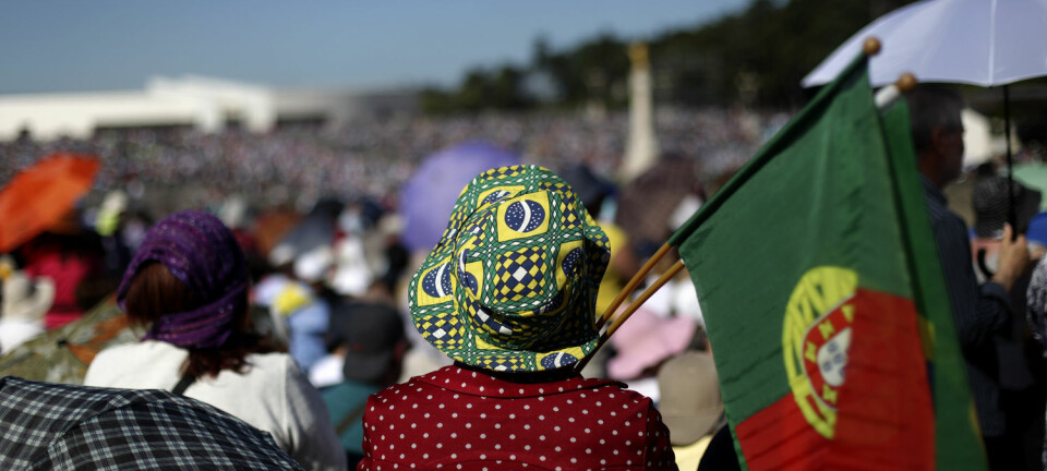 En kvinne med hatt med det brasilianske flagget på holder et portugisisk flagg under en pilgrimstur i Portugal. (Foto: AP Photo, Francisco Seco, NTB Scanpix)