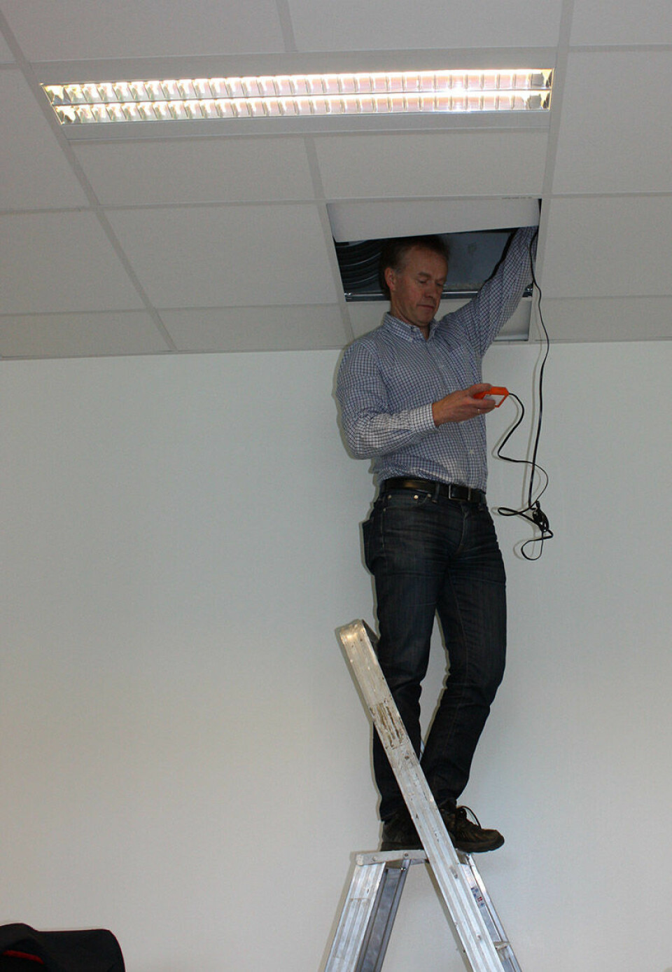 Ikke alt lar seg gjøre via fjernkontroll. Prosjektkoordinator Mads Mysen fra Sintef må stikke hodet opp i taket for å programmere spjeldene som kontrollerer ventilasjonen i klasserommet. (Foto: NILU)