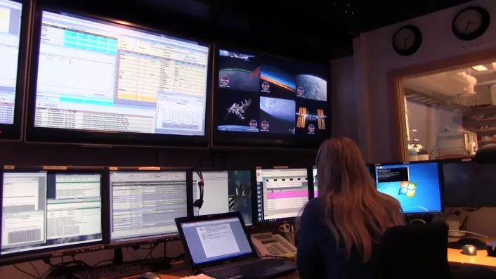 Mona Schiefloe har sittet ved denne konsollen hele dagen, og fulgt med på hva som har skjedd på romstasjonen på skjermene bak. Videolinken har vært på den seksdelte skjermen midt i bildet. (Foto: Lasse Biørnstad/forskning.no)