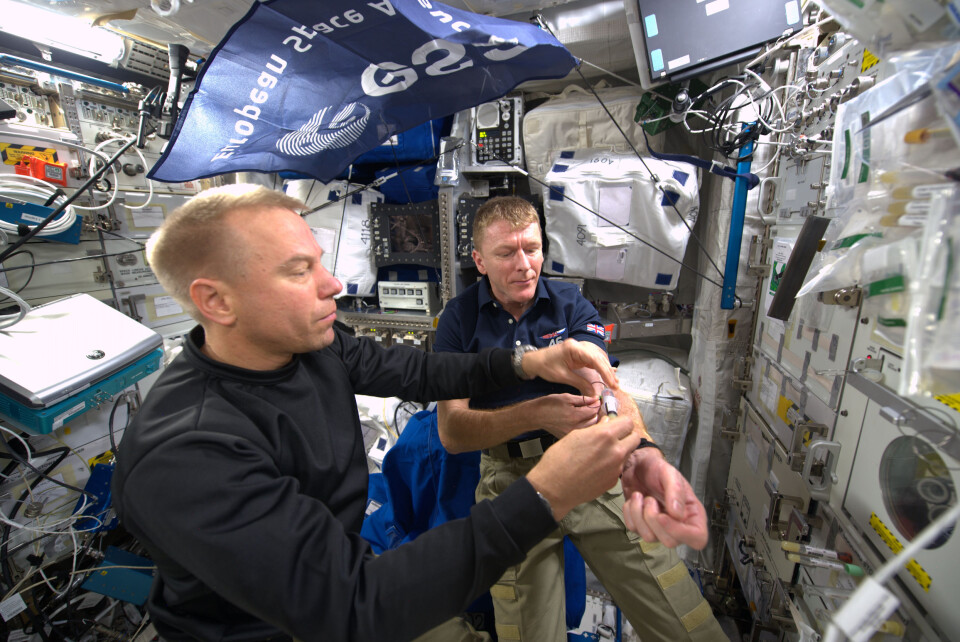 Her får Tim Peake (t.h.), ESAs britiske astronaut, tatt en blodprøve av NASAs astronaut Tim Kopra i 2015. (Foto: ESA/NASA)