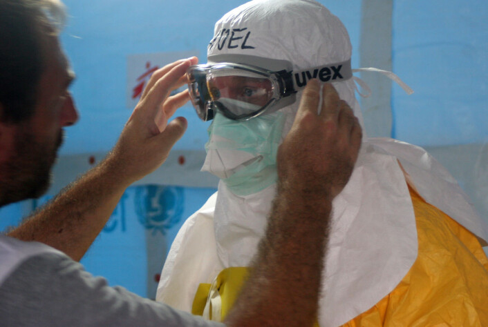 Dr. Joel Montgomery fra organisasjonen Leger uten grenser får hjelp med smittevernet av kollega i en behandlingsenhet i Vest-Afrika, 27. august 2014. Leger uten grenser kritiserte WHO for sein og dårlig innsats da epidemien vokste katastrofalt utover seinsommeren og høsten 2014. (Foto: Athalia Christie, Creative Commons Attribution 2.0 Generic license) Dr. Joel Montgomery fra organisasjonen Leger uten grenser får hjelp med smittevernet av kollega i en behandlingsenhet i Vest-Afrika, 27. august 2014. Leger uten grenser kritiserte WHO for sein og dårlig innsats da epidemien vokste katastrofalt utover seinsommeren og høsten 2014. (Foto: Athalia Christie, Creative Commons Attribution 2.0 Generic license)