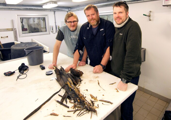 Geir Johnsen (til venstre), Jørgen Berge og Øyvind Ødegård undersøker trestokken om bord på forskningsskipet «Helmer Hanssen». (Foto: UiT) Geir Johnsen (til venstre), Jørgen Berge og Øyvind Ødegård undersøker trestokken om bord på forskningsskipet «Helmer Hanssen». (Foto: UiT)