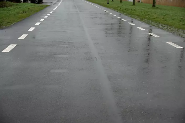 Etter et halvt år ser det ut til å være forskjeller: Til venstre på veien, der det ligger vanlig asfalt, har slitasjen laget dumper der vannet legger seg på en regnværsdag, mens bioasfalten til høyre på bildet ikke har den samme slitasjen. (Foto: Georg Mathisen)