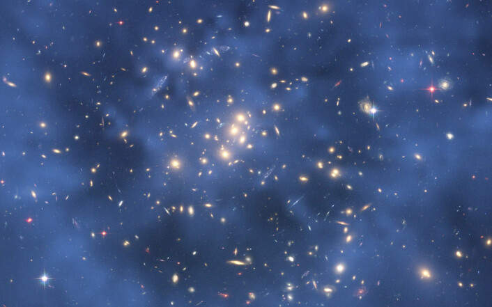 Ett av foreløpig de sterkeste bevisene på mørk materie er denne spøkelsesaktige ringen etter en gigantisk kollisjon mellom to galaksehoper. Ringen er ikke synlig, men tegnet inn på dette bildet tatt av romteleskopet Hubble for å vise fordelingen av den mørke materien. Den mørke materien kan bare indirekte påvises ved å studere hvordan lyset avbøyes av tyngdekraften fra den mørke materien i galaksehopene. (Foto: NASA, ESA, M.J. Jee og H. Ford, Johns Hopkins University)