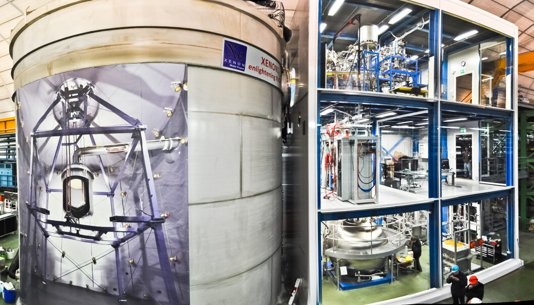 Xenon1T er plassert i en hule som måler 100x20x18 meter. Plakaten på den store vanntanken viser innholdet – selve detektoren sitter inne i midten av tanken. Den gjennomsiktige bygningen ved siden av rommer blant annet kjølesystemet. (Foto: The Xenon Collaboration) Xenon1T er plassert i en hule som måler 100x20x18 meter. Plakaten på den store vanntanken viser innholdet – selve detektoren sitter inne i midten av tanken. Den gjennomsiktige bygningen ved siden av rommer blant annet kjølesystemet. (Foto: The Xenon Collaboration)
