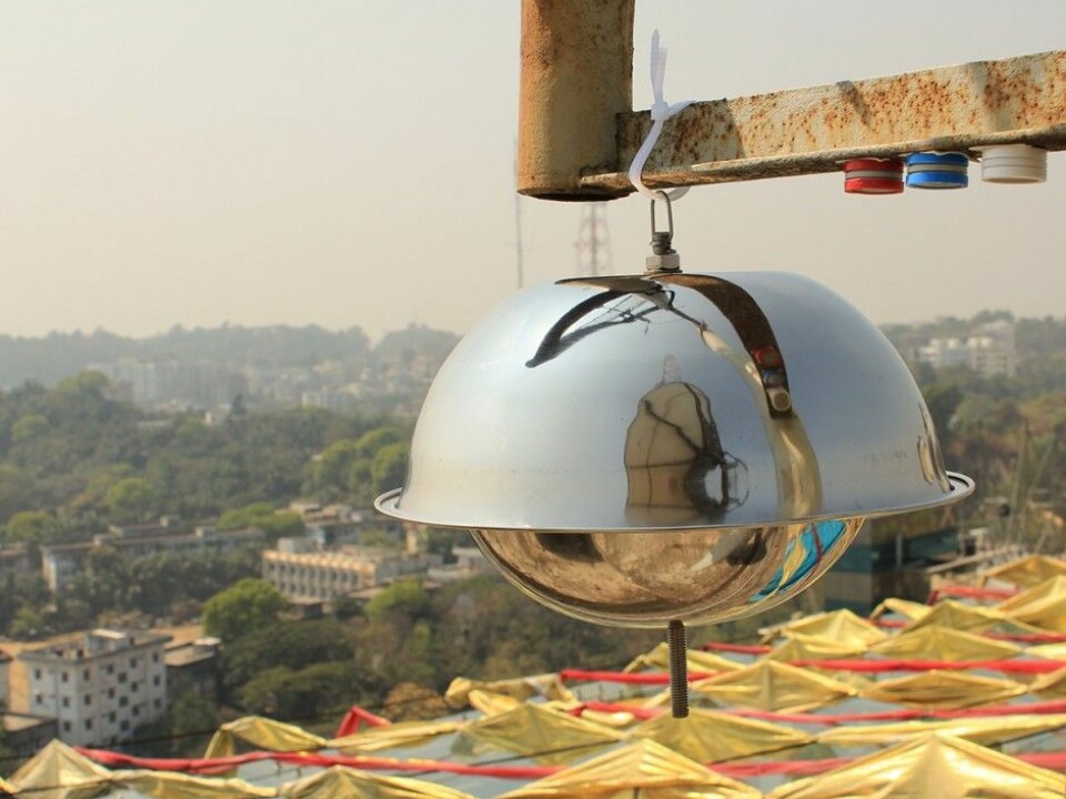 The image shows air samplers in the city of Chittagong in Bangladesh. The large 'metal dome' collects air samples for analysis of environmental pollutants, while the three small cylinders measure nitrogen dioxide (blue), sulfur dioxide (red) and ozone (white). (Photo: Scott Randall, NILU)