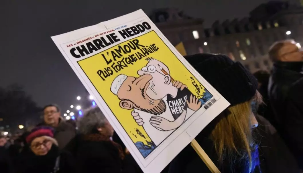 En kvinne holder en plakat av en Charlie Hebdo-forside med teksten «Kjærlighet sterkere enn hat». Bildet ble tatt under markeringen på Place de la Republique i Paris 7. januar 2015, etter angrepet på redaksjonen til satiremagasinet Charlie Hebdo der 12 mennesker ble drept. (Foto: Scanpix, Dominique Faget)