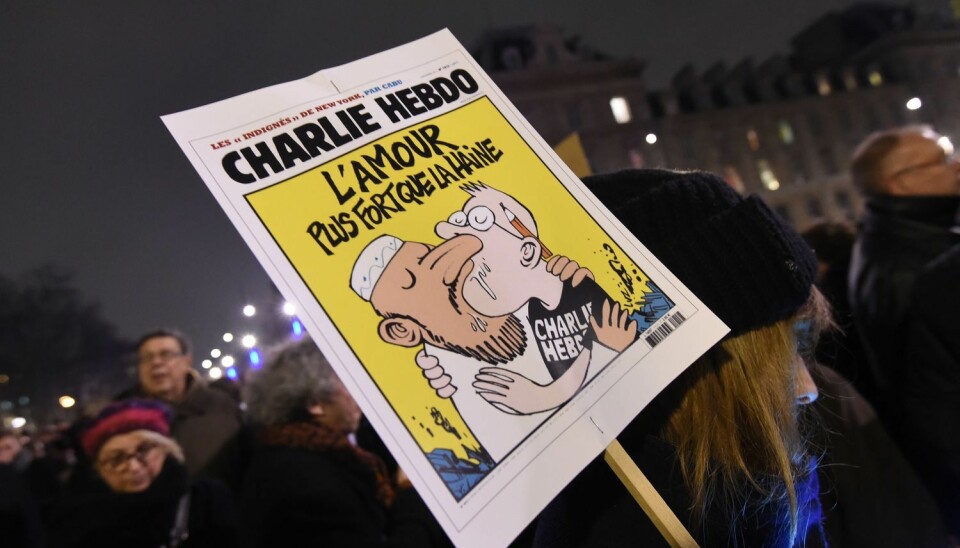 En kvinne holder en plakat av en Charlie Hebdo-forside med teksten Kjærlighet sterkere enn hat. Bildet ble tatt under markeringen på Place de la Republique i Paris 7. januar 2015, etter angrepet på redaksjonen til satiremagasinet Charlie Hebdo der 12 mennesker ble drept.   (Foto: Scanpix, Dominique Faget)