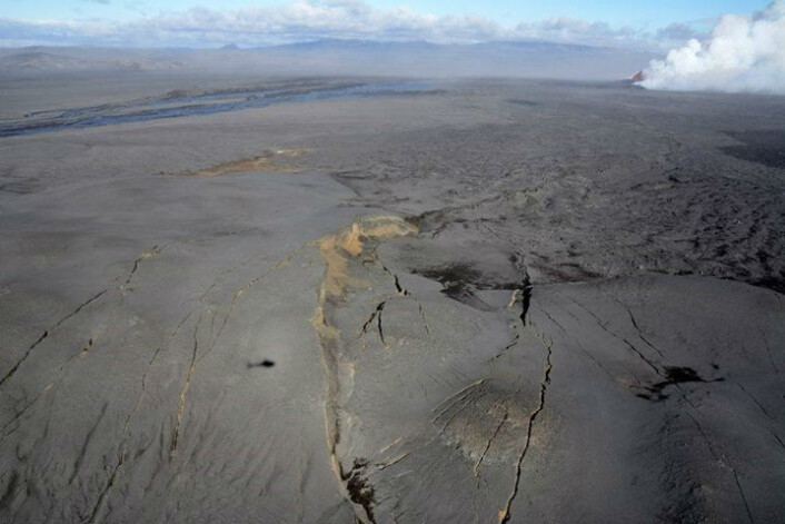 Fig. 6. Western margin of a 600-800 m wide and 6 km long graben NNE of and under Dyngjujökull (looking northwards). Dyngjufjöll, with the Askja central volcano, is on the horizon in the north. Upper right: the erupting crater row (fire fountain and gas cloud), 2-3 km further SSW: short-lived satellite lava field (black colour at the right edge). Photo: Morgan Jones, Centre for Earth Evolution and Dynamics, University of Oslo, Sept. 10. Note the shadow of Morgan's helicopter slightly west of the main western normal fault (see detailed view in Fig. 7). Fig. 6. Western margin of a 600-800 m wide and 6 km long graben NNE of and under Dyngjujökull (looking northwards). Dyngjufjöll, with the Askja central volcano, is on the horizon in the north. Upper right: the erupting crater row (fire fountain and gas cloud), 2-3 km further SSW: short-lived satellite lava field (black colour at the right edge). Photo: Morgan Jones, Centre for Earth Evolution and Dynamics, University of Oslo, Sept. 10. Note the shadow of Morgan's helicopter slightly west of the main western normal fault (see detailed view in Fig. 7).