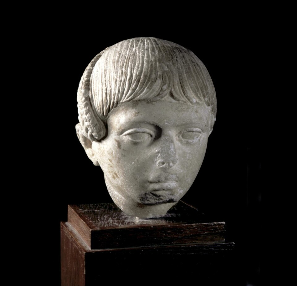 Skulptur av romersk gutt med hår i Egyptisk stil med såkalt Horus-lokk. Lokken ble klippet av og forært til gudene i forbindelse med festen som markerte overgangen til voksenlivet. Første halvdel av 2. århundre e.Kr.  (Foto: Kulturhistorisk museum)