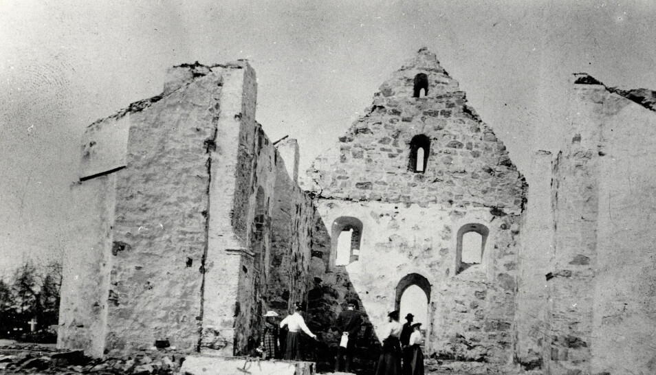 Mennesker midt i ruinene av Øyestad kirke før den ble gjenoppbygd. (Foto: Riksantikvarens billeddatabase, kulturminnebilder.ra.no)