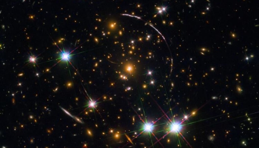 A Hubble Space Telescope photo of a massive galaxy cluster, about 4.6 billion light years away. Along its borders four bright arcs are visible; these are copies of the same distant galaxy, nicknamed the Sunburst Arc Galaxy. Photo: ESA/NASA/Rivera-Thorsen A Hubble Space Telescope photo of a massive galaxy cluster, about 4.6 billion light years away. Along its borders four bright arcs are visible; these are copies of the same distant galaxy, nicknamed the Sunburst Arc Galaxy. Photo: ESA/NASA/Rivera-Thorsen