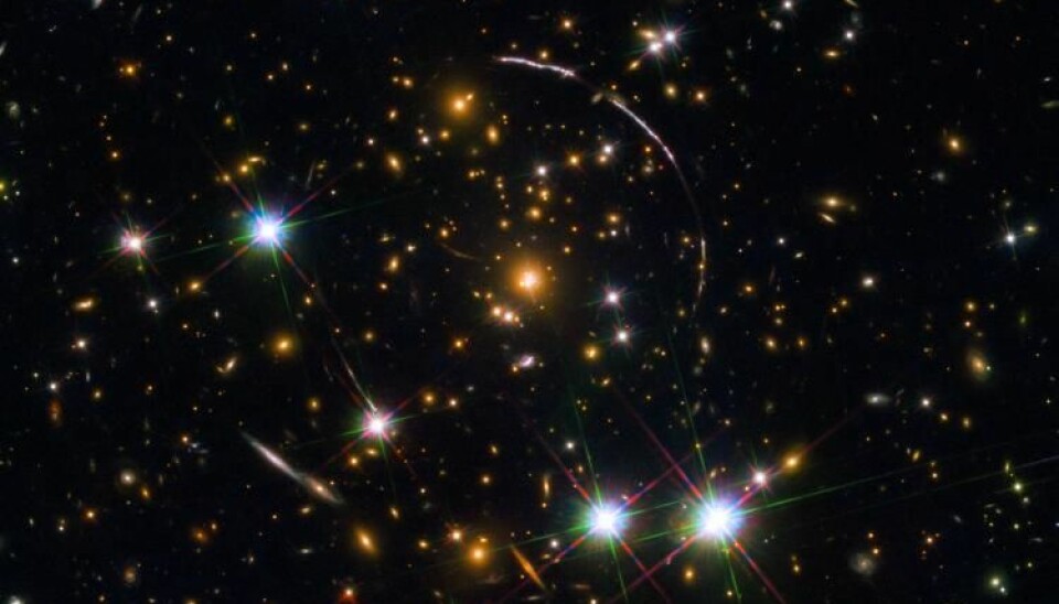 A Hubble Space Telescope photo of a massive galaxy cluster, about 4.6 billion light years away. Along its borders four bright arcs are visible; these are copies of the same distant galaxy, nicknamed the Sunburst Arc Galaxy. Photo: ESA/NASA/Rivera-Thorsen