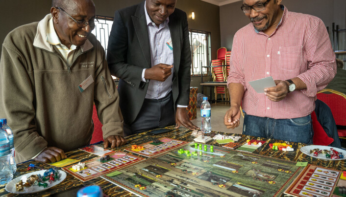 Players stand around a game board as it is being set up. Players stand around a game board as it is being set up.