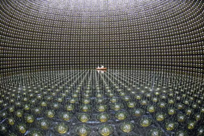 Den japanske nøytrino-detektoren Super-Kamiokande inneholder 50 millioner liter vann. De runde objektene er lysdetektorene som registrerer lysglimt etter sjeldne nøytrinokollisjoner. I midten seiler et par teknikere rundt i en gummibåt. (Foto: Kamioka Observatory)