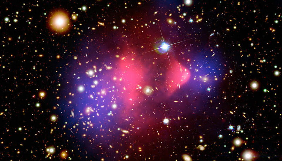 Det røde området i midten viser røntgenstråling fra to kolliderende galaksehoper, fotografert med romteleskopet Chandra. Vanlig materie ble bremset opp i kollisjonen (rødt), mens den mørke materien fortsatte tvers gjennom, upåvirket (blått). Den mørke materien er tegnet inn i fotografiet, da den ikke kunne påvises direkte, bare måles ut fra hvordan tyngdekreftene deres avbøyde lysstråler fra galaksene. NASA/CXC/M. Weiss