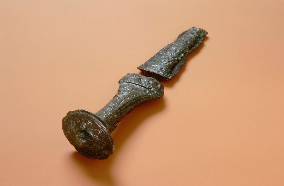 Dette bronsehåndtaket til en dolk eller et sverd ble funnet i en gravhaug på Nærbø i Rogaland. Det har trekk fra Mykene i Hellas. Samtidig ligner det også et håndtak fra Schleswig-Holstein i Tyskland.