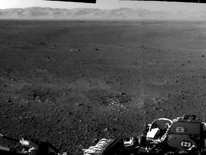 Dette er et av de første høyoppløselige bildene fra Mars-overflaten, tatt av et av navigasonskameraene på Curiosity. Blant annet kan kanten på Gale Crater ses i bakgrunnen, bortenfor den ellers småteinete overflaten. Samtidig ser vi mer i front av bildet avtrykk etter rakettene fra landingsfartøyet som hjalp Mars-roveren den siste biten ned til den røde planet. (Foto: NASA/JPL-Caltech)