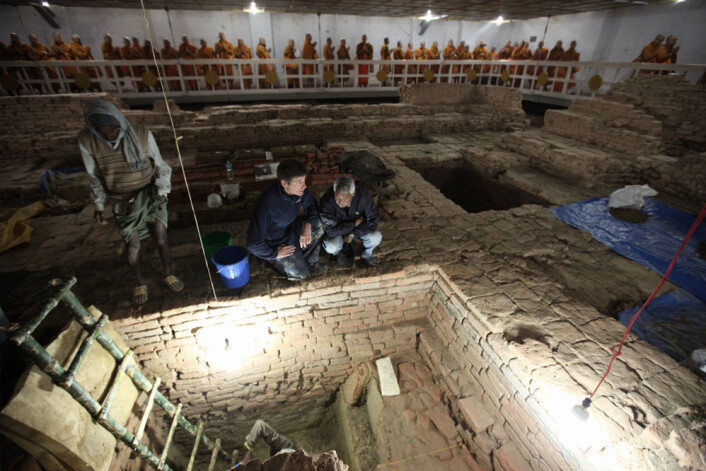 Arkeolog Robin Coningham (t.v.) og Kosh Prasad Acharya styrer utgravningene inne i Maya Devi-tempelet. Fram fra jorda kommer rester etter eldgamle templer fra Buddhaens egen tid. I bakgrunnen mediterer munker. (Foto: Ira Block/National Geographic) Arkeolog Robin Coningham (t.v.) og Kosh Prasad Acharya styrer utgravningene inne i Maya Devi-tempelet. Fram fra jorda kommer rester etter eldgamle templer fra Buddhaens egen tid. I bakgrunnen mediterer munker. (Foto: Ira Block/National Geographic)