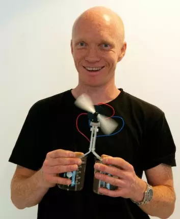 Ole Martin Løvvik demonstrerer termoelektrisitet med ett glass kaldt og ett glass varmt vann. Den nye teknologien utnytter temperaturforskjellen og gir energi til en hurtig roterende vifte. (Foto: Yngve Vogt)