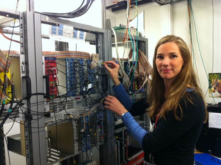 Forsker Ann Cecilie Larsen ved elektronikkboksene i datarommet på UiO. Her behandles signalene fra måleinstrumentene i eksperimenthallen. (Foto: Trine W. Hagen) Forsker Ann Cecilie Larsen ved elektronikkboksene i datarommet på UiO. Her behandles signalene fra måleinstrumentene i eksperimenthallen. (Foto: Trine W. Hagen)