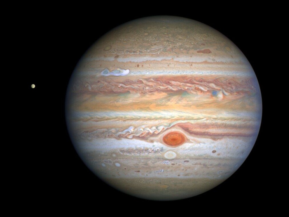 Jupiter som vi kjenner den, med den karakteristiske røde flekken, en storm som er 2–3 ganger større enn jorden, samt en ny, hvit stormsky som er synlig i den øvre siden av planeten. Til venstre for Jupiter ser vi ismånen Europa. Jupiter som vi kjenner den, med den karakteristiske røde flekken, en storm som er 2–3 ganger større enn jorden, samt en ny, hvit stormsky som er synlig i den øvre siden av planeten. Til venstre for Jupiter ser vi ismånen Europa.