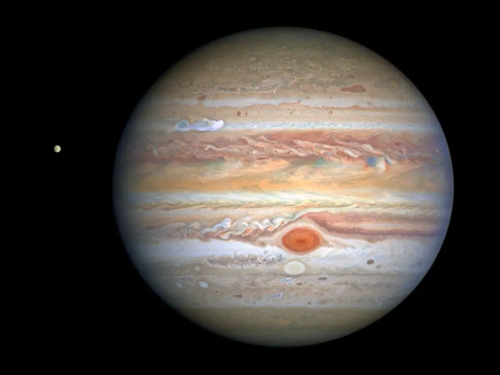Jupiter som vi kjenner den, med den karakteristiske røde flekken, en storm som er 2–3 ganger større enn jorden, samt en ny, hvit stormsky som er synlig i den øvre siden av planeten. Til venstre for Jupiter ser vi ismånen Europa. Jupiter som vi kjenner den, med den karakteristiske røde flekken, en storm som er 2–3 ganger større enn jorden, samt en ny, hvit stormsky som er synlig i den øvre siden av planeten. Til venstre for Jupiter ser vi ismånen Europa.
