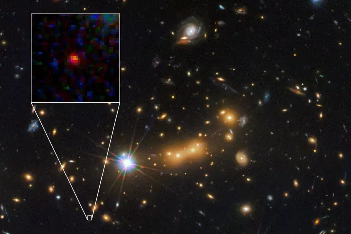 Den ser bare ut som en liten, rød dott på bildet, men det er en hel galakse; langt, langt unna vår egen klode. (Foto: NASA, ESA; M. Postman og D. Coe (Space Telescope Science Institute); samt CLASH-teamet)