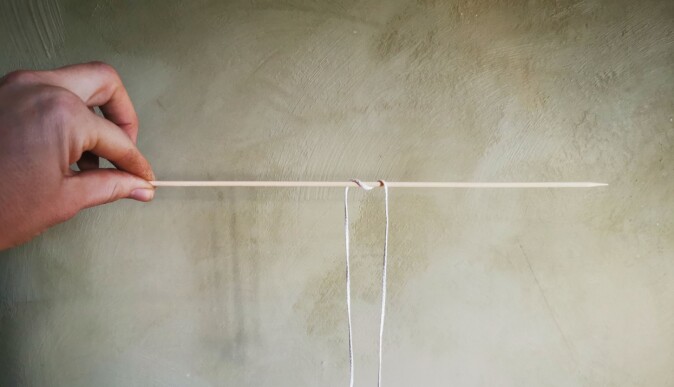 Heng veken over et trespyd eller en pinne og la den henge ned et stykke på begge sider. Bind en mutter i enden, så synker den til bunns i bivoksen og lyset holder seg rett. Heng veken over et trespyd eller en pinne og la den henge ned et stykke på begge sider. Bind en mutter i enden, så synker den til bunns i bivoksen og lyset holder seg rett.