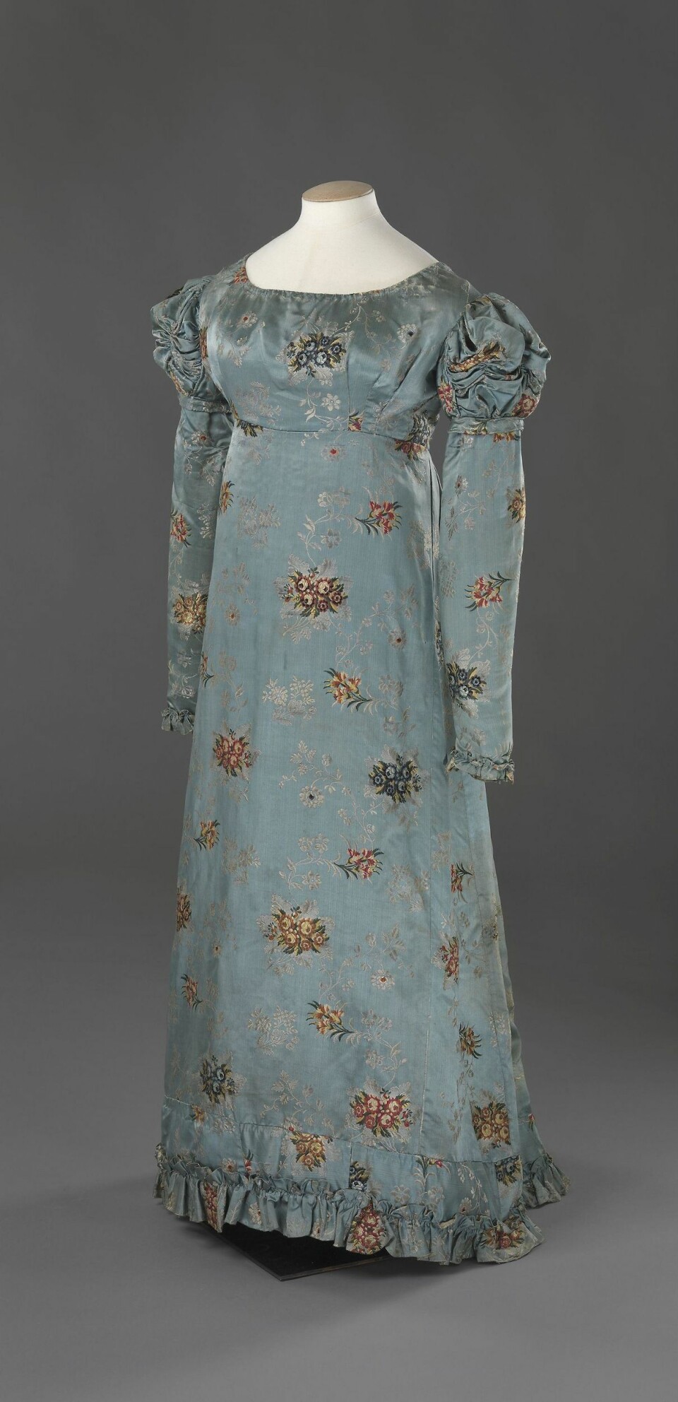 Denne kjolen er fra første halvdel av 1820-tallet og ble sannsynligvis brukt av den lille eliten i Norge. Kjolen er laget av stoff fra 1700-tallet, og trolig omsydd fra en eldre kjole. Det er blant annet mye skjøting i skjørtekanten. (Foto: Nasjonalmuseet for kunst, arkitektur og design)