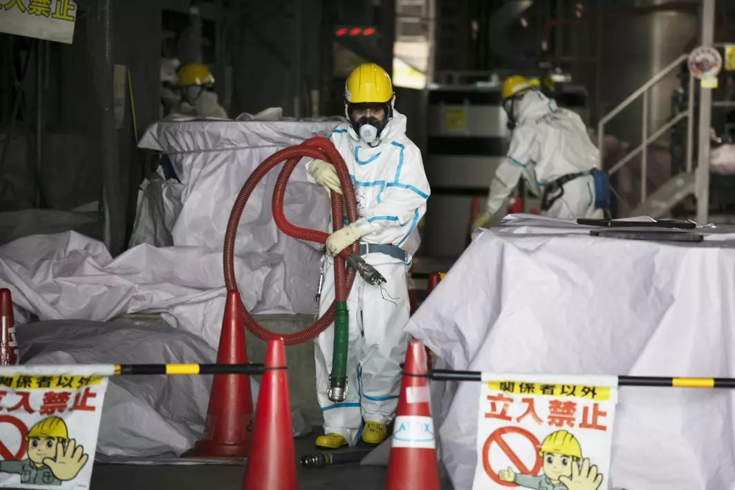 Arbeidere med beskyttelsesdresser jobber ved den ødelagte atomkraftverket Fukushima Daiichi i Japan. Arbeidet med å rydde opp og avvikle atomkraftverket etter katastrofen vil ta 30–40 år og koste enorme beløp.