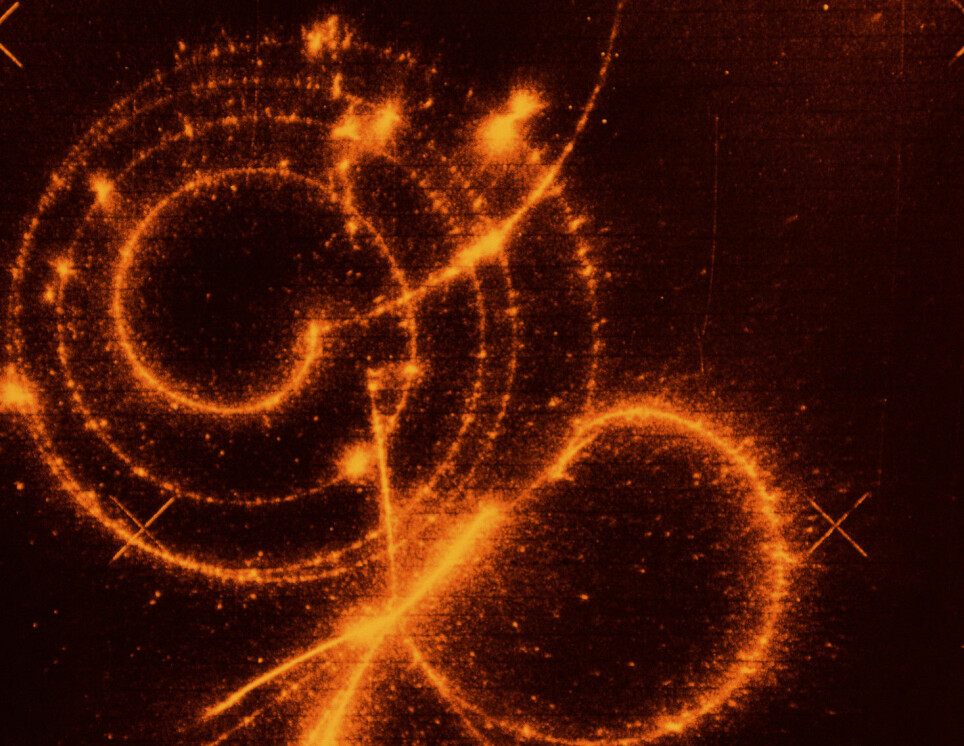 Dette er et bilde fra et CERN-eksperiment fra 1970-tallet som viser forskjellige partikkelbaner i en partikkeldetektor. En kraftig partikkelkollisjon henfaller til flere andre partikler, blant annet et myon. Myonet lager den karakteristiske spiralen du ser midt i bildet. Der spiralen slutter har myonet henfalt til et elektron, som skyter ut til høyre. Myonet henfaller også til nøytrinoer, men disse partiklene blir ikke plukket opp av detektoren.