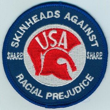 "Jakkemerke fra Skinheads Against Racial Prejudice, prydet av emblemet til reaggeselskapet Trojan." "Jakkemerke fra Skinheads Against Racial Prejudice, prydet av emblemet til reaggeselskapet Trojan."