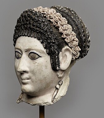 Kvinnehode fra det romerske Egypt, 1. årh. e.Kr. Hodet har sittet på en mumiekiste. Kvinnens frisyre er inspirert av moten blant kvinnene i den flaviske keiserfamilien. Luggen høyt oppsatt med krøller, det lange håret sirlig flettet og bundet i en stor knute. Som hårpynt har hun en krans i rosa farge. Kvinnehode fra det romerske Egypt, 1. årh. e.Kr. Hodet har sittet på en mumiekiste. Kvinnens frisyre er inspirert av moten blant kvinnene i den flaviske keiserfamilien. Luggen høyt oppsatt med krøller, det lange håret sirlig flettet og bundet i en stor knute. Som hårpynt har hun en krans i rosa farge.