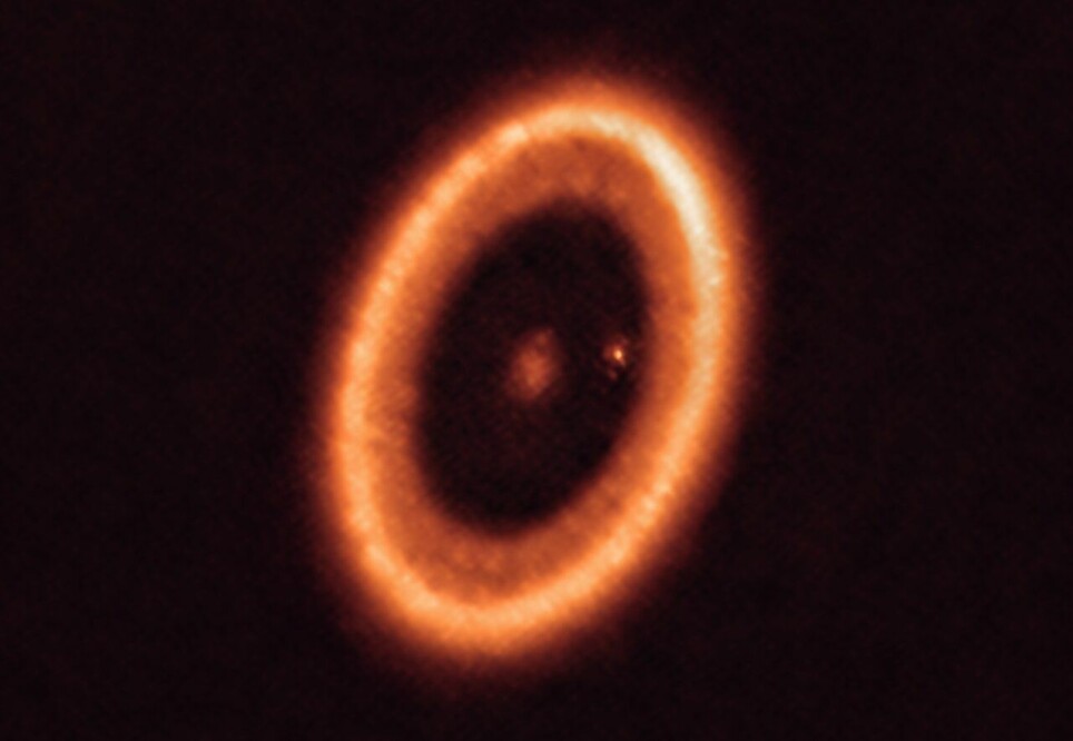 Bildet viser hele det fremmede solsystemet, med stjernen i midten. Rundt ser vi skiven med gass og støv som omgir stjernen. Den lille lysende prikken er en planet. Den har samlet opp det meste av gass og støv i området inn mot stjernen. Derfor er det blitt en tom, sort ring i skiven.