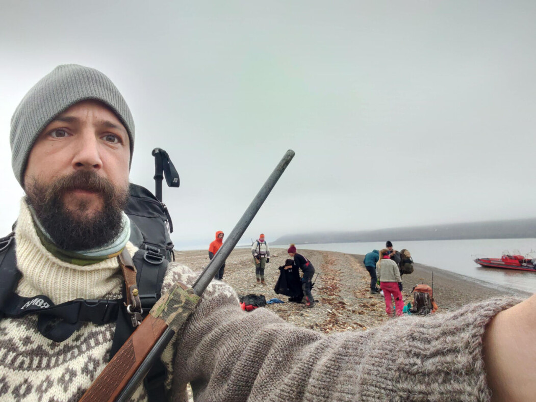 Selfie av prosjektleiar Sam Steyaert med felt-teamet i bakgrunnen. Bilete er tatt i Hiorthhamn medan dei ventar på båtskyss attende til Longyearbyen etter end arbeidsdag. Selfie av prosjektleiar Sam Steyaert med felt-teamet i bakgrunnen. Bilete er tatt i Hiorthhamn medan dei ventar på båtskyss attende til Longyearbyen etter end arbeidsdag.