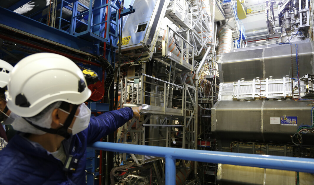 Forsker Alex Tuna peker inn i en ufattelig haug med teknologi. Der inne bak stillaset sitter en del av detektoren som han selv har vært med på å lage. Delen kalles det lille hjulet, men i virkeligheten er det gigantiske ti meter i diameter. (Munnbindet har ingenting med lufta i ATLAS i gjøre, men er påbudt ved hele CERN som et tiltak mot koronasmitte.)