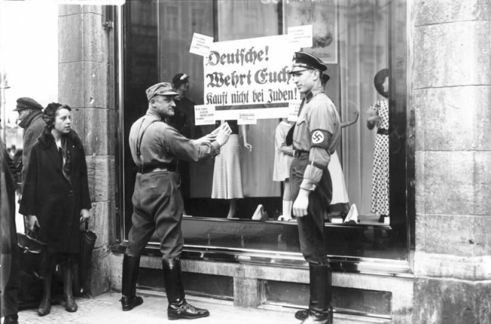 Berlin 1933: Nazister henger opp et skilt med teksten: 'Tyskere, forsvar dere, ikke kjøp hos jøder' på et jødisk butikkvindu. (Foto: Deutsches Bundesarchiv / Wikimedia commons)