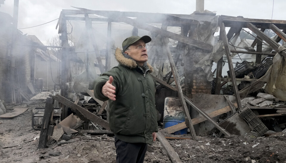 En mann åpner armene foran et hus som er ødelagt av russisk artilleri i Horenka utenfor Kyiv.
