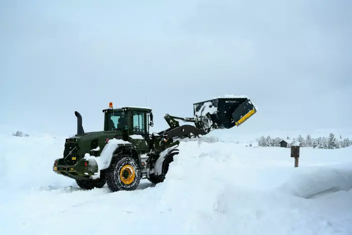 A front-loader is used to pour snow over the mannequin.