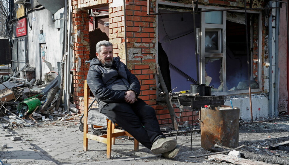 En mann sitter utenfor en bombet bygning i Mariuopol øst i Ukraina.