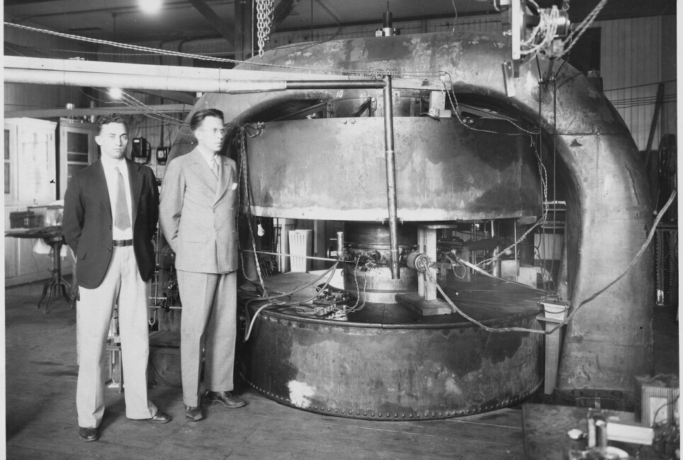 Stanley Livingston og Ernest Lawrence fotografert i 1934. Forskerne står foran en nesten 70 centimeter bred syklotronsom kunne akselerere partikler opp til 4,8 millioner elektronvolt.