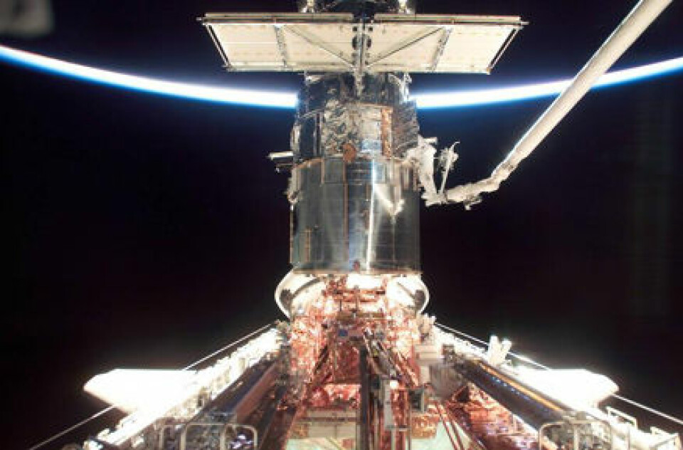 'Hubble repareres i 2002, med jordkloden som kommer frem i lyset i bakgrunnen. En astronaut jobber med halve kroppen inne i romteleskopet.'