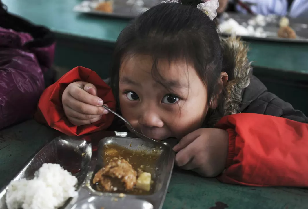 Ei jente spiser skolelunsj. Mange barn har fulgt med fattige migrantarbeidere som de siste tiårene har flyttet fra landsbygda til kinesiske byer.